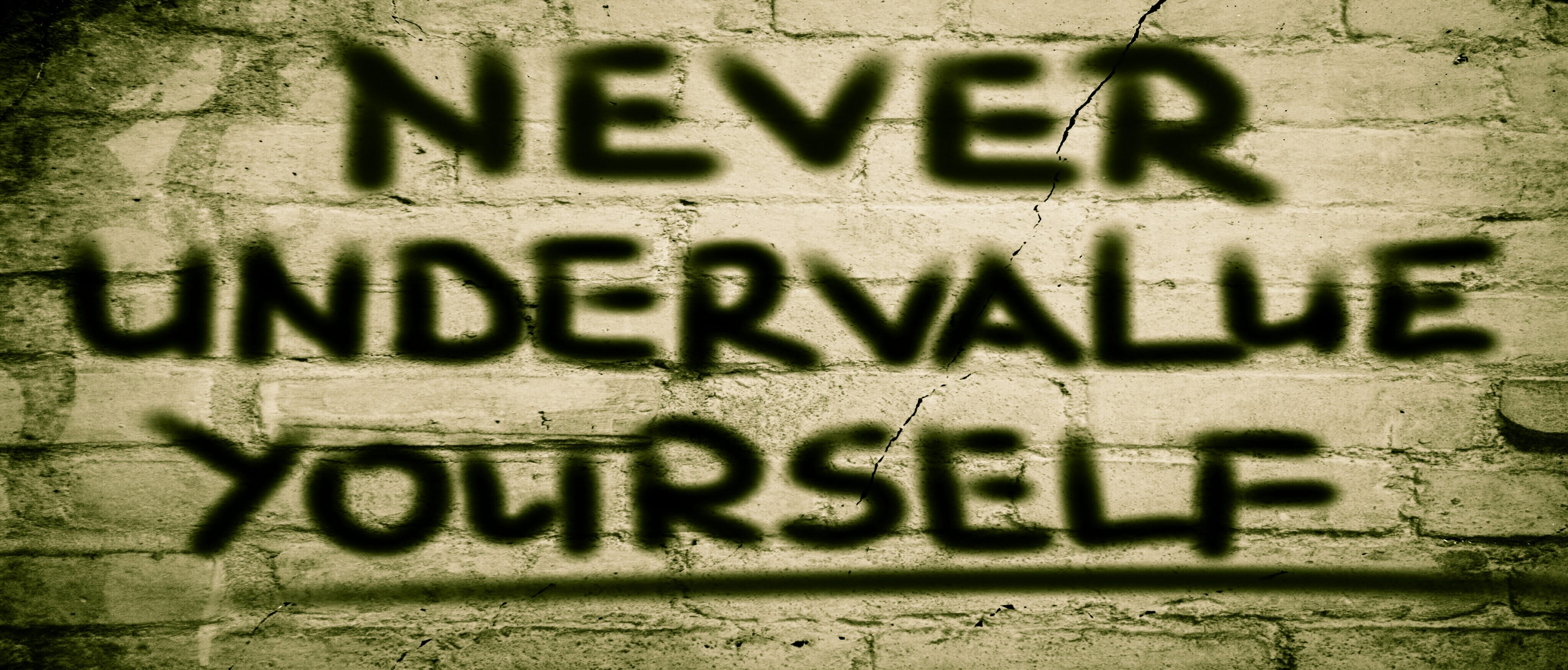 Graffiti on a wall saying 'Never Underestimate Yourself'.